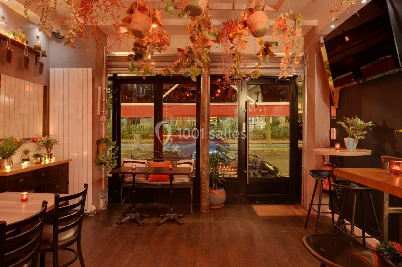 Salle de restaurant chaleureuse avec décoration végétale suspendue, éclairage tamisé et mobilier en bois.