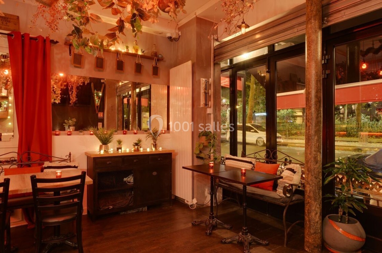 Intérieur d'un café chaleureux avec éclairage tamisé, plantes suspendues et grandes fenêtres donnant sur la rue.