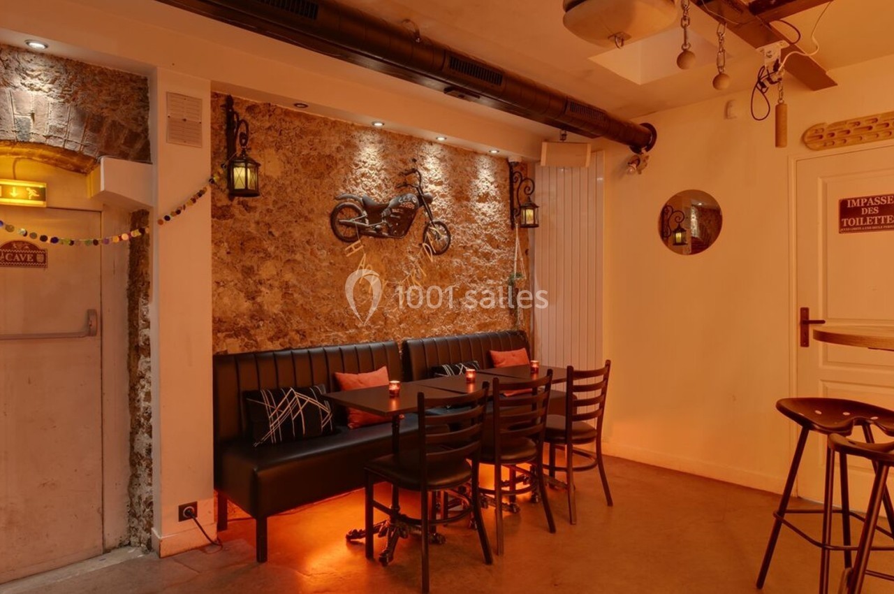 Salle chaleureuse avec murs en pierre, banquette, table et chaises en bois, éclairage tamisé et décoration murale.