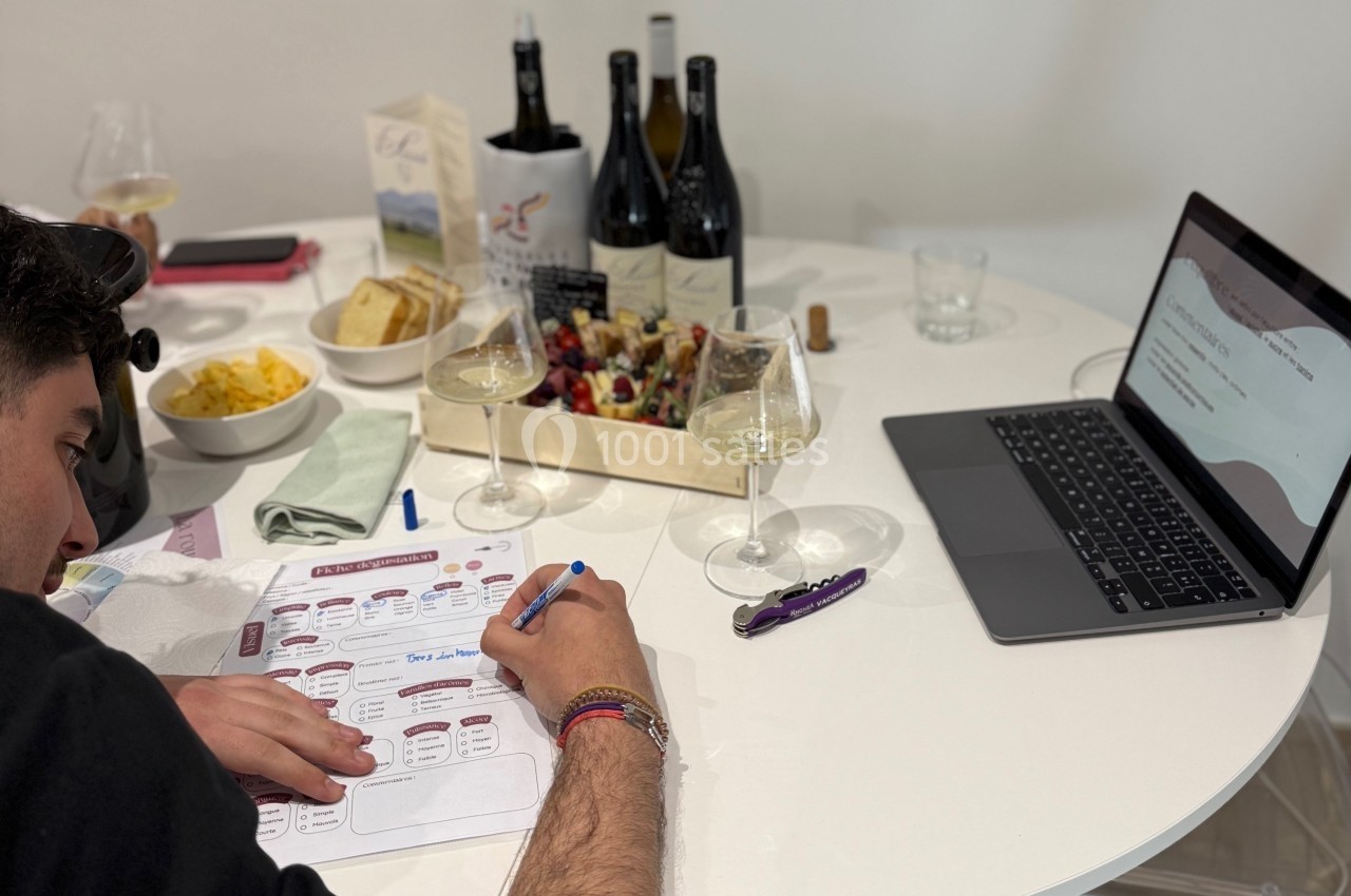 Un homme remplit un document à une table avec des verres de vin, un ordinateur portable et un plateau apéritif.
