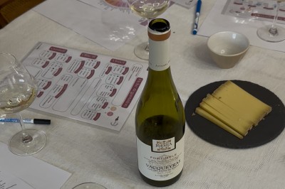 Bouteille de vin blanc, verres, assiette de carpaccio et documents de dégustation sur une table dressée.