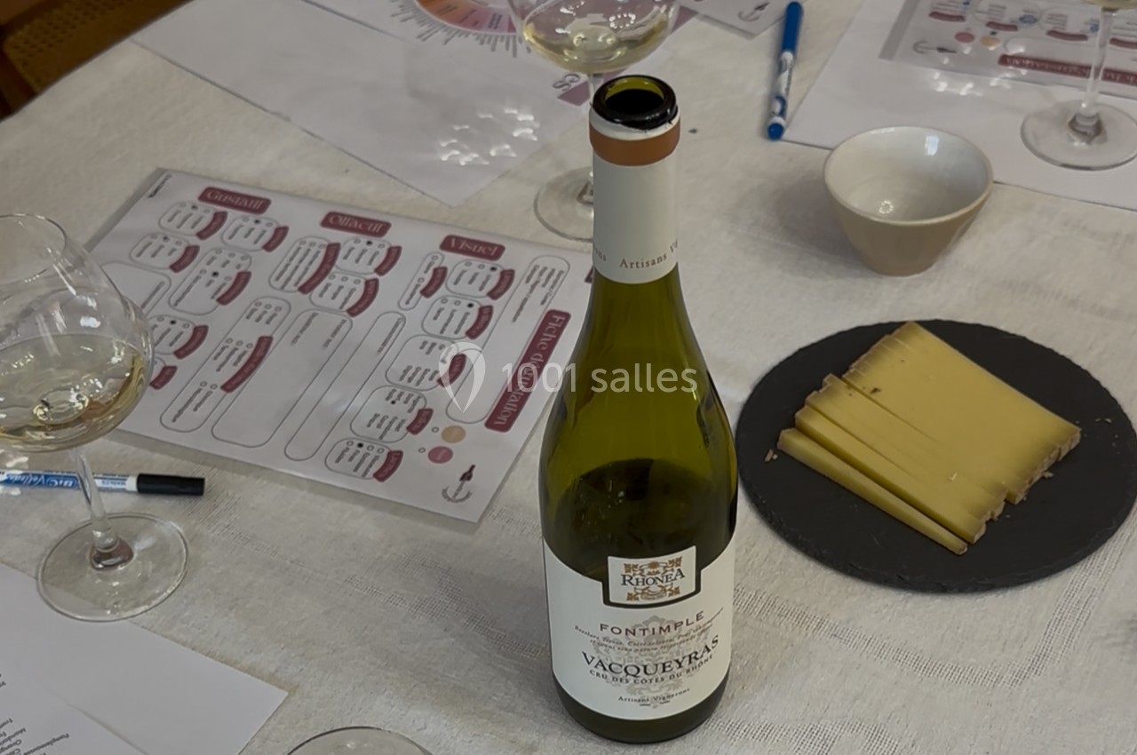 Bouteille de vin blanc Vacqueyras sur une table avec verres, assiette de fromage et documents de dégustation.