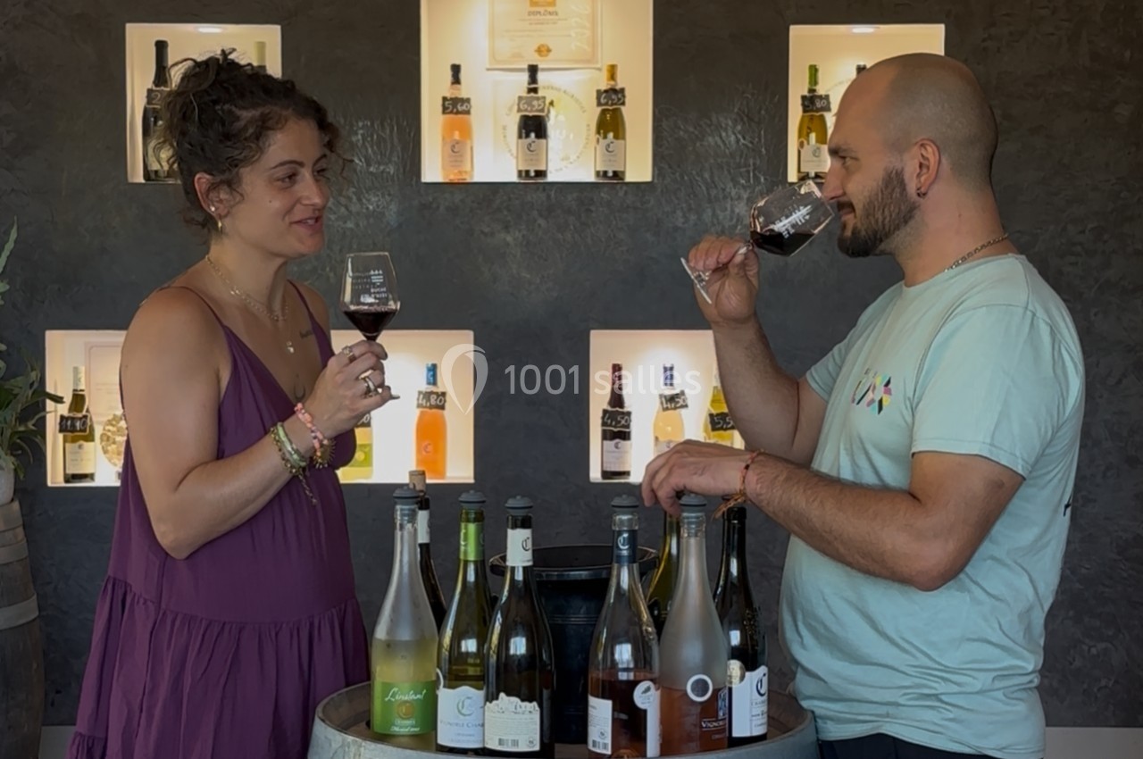 Deux personnes dégustent du vin rouge devant un présentoir de bouteilles éclairées.