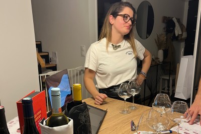 Bouteille de vin blanc, verres, assiette de carpaccio et documents de dégustation sur une table dressée.