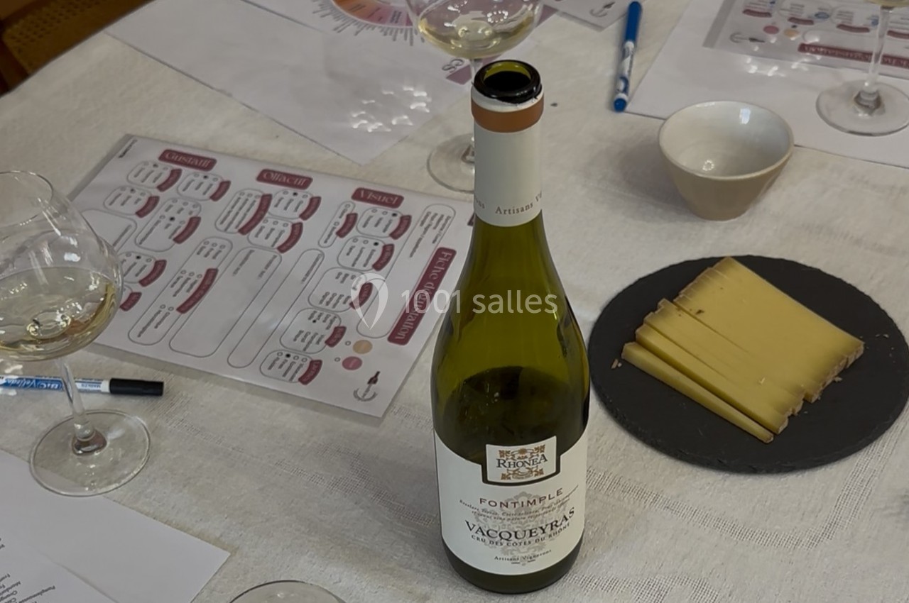 Bouteille de vin blanc, verres, assiette de fromage et documents sur une table lors d'une dégustation.