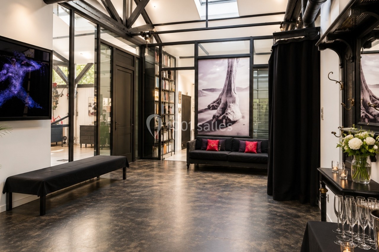 Espace intérieur moderne avec sol en béton, canapé noir, œuvres d'art murales et table avec flûtes de champagne.