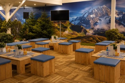 Espace de détente avec bancs et tables en bois, décor alpin avec montagnes en arrière-plan et éclairage chaleureux.