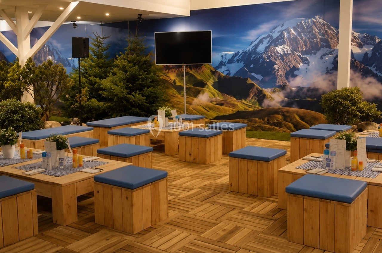 Salle aménagée avec des tables et bancs en bois, décorée de plantes et d'une fresque murale représentant des montagnes.