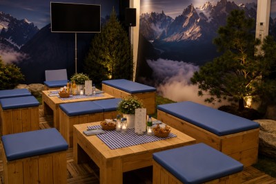 Espace de détente avec bancs et tables en bois, décor alpin avec montagnes en arrière-plan et éclairage chaleureux.