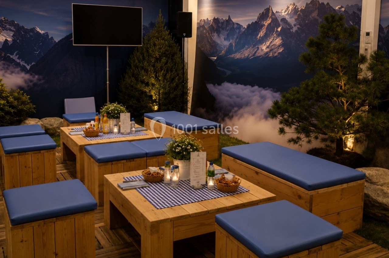 Espace de détente avec bancs et tables en bois, décor alpin avec montagnes en arrière-plan et éclairage chaleureux.
