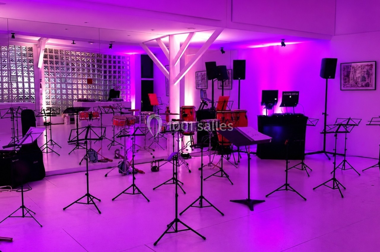 Salle de répétition avec des pupitres, instruments de musique et éclairage violet.