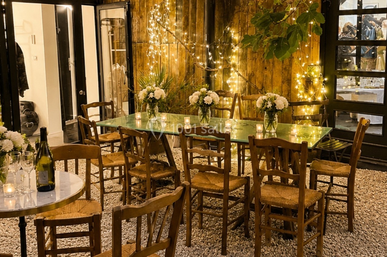 Terrasse éclairée avec des guirlandes lumineuses, tables en bois, chaises en paille et bouquets de fleurs blanches.