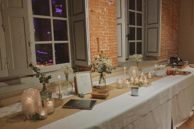 Grande table en bois dressée avec vaisselle, bougies et décorations, dans une salle au mur de briques et sol en terre cuite.