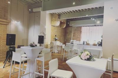 Grande table en bois dressée avec vaisselle, bougies et décorations, dans une salle au mur de briques et sol en terre cuite.