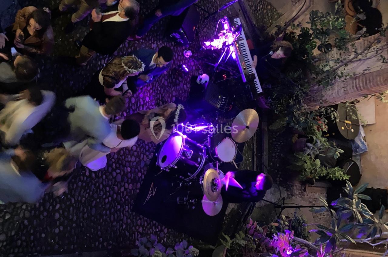 Vue aérienne d'une scène musicale en extérieur avec batterie, clavier et éclairage violet, entourée de spectateurs.