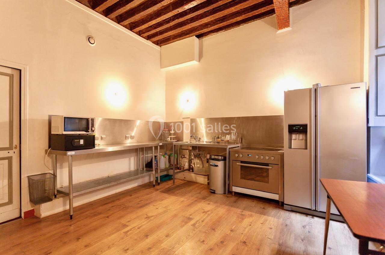 Cuisine avec plancher en bois, plafond à poutres apparentes, équipements en inox, réfrigérateur et micro-ondes.