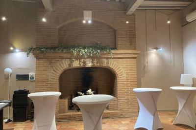 Grande table en bois dressée avec vaisselle, bougies et décorations, dans une salle au mur de briques et sol en terre cuite.