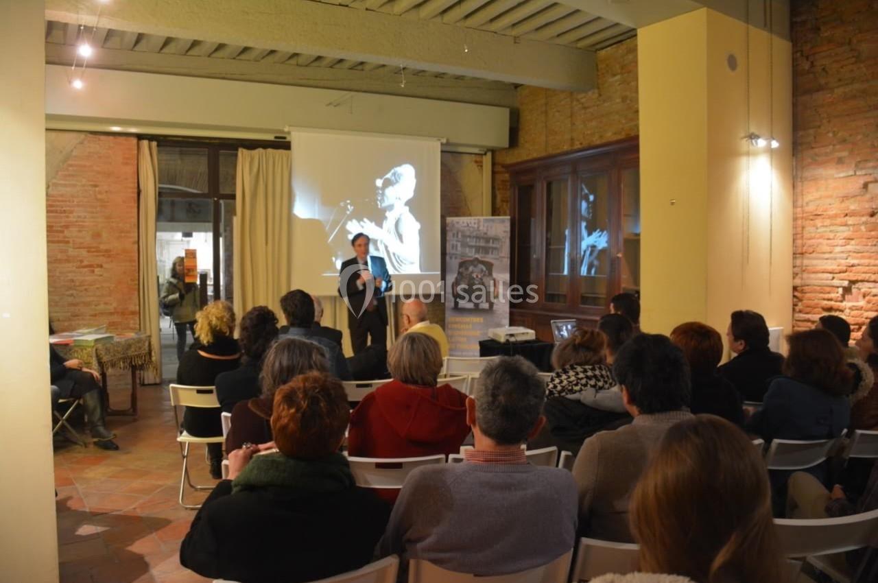 Un conférencier s'adresse à un public assis dans une salle avec projection d'une image en noir et blanc.