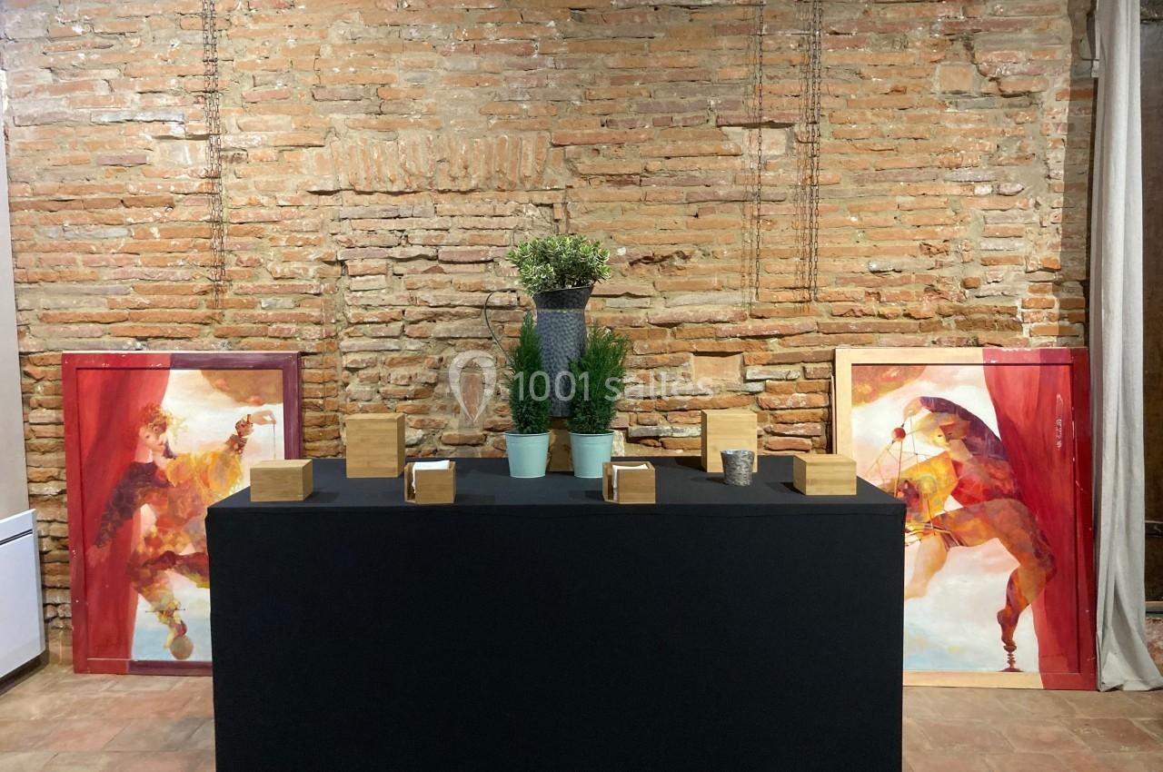 Table noire décorée de plantes en pots et de petits objets en bois, devant un mur de briques avec deux tableaux colorés.