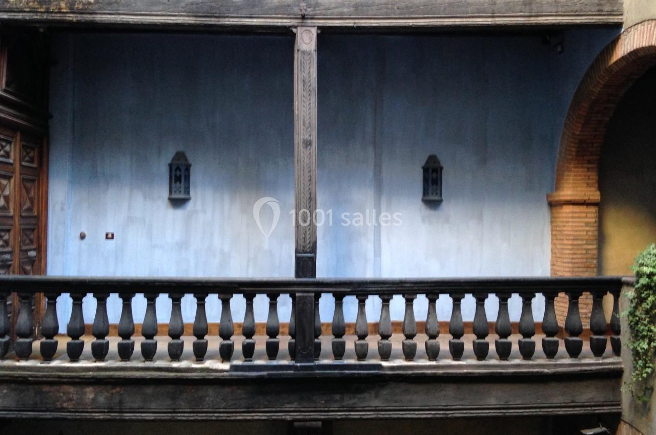 Balustrade en bois sombre devant un mur bleu avec deux lanternes murales et des éléments en briques.