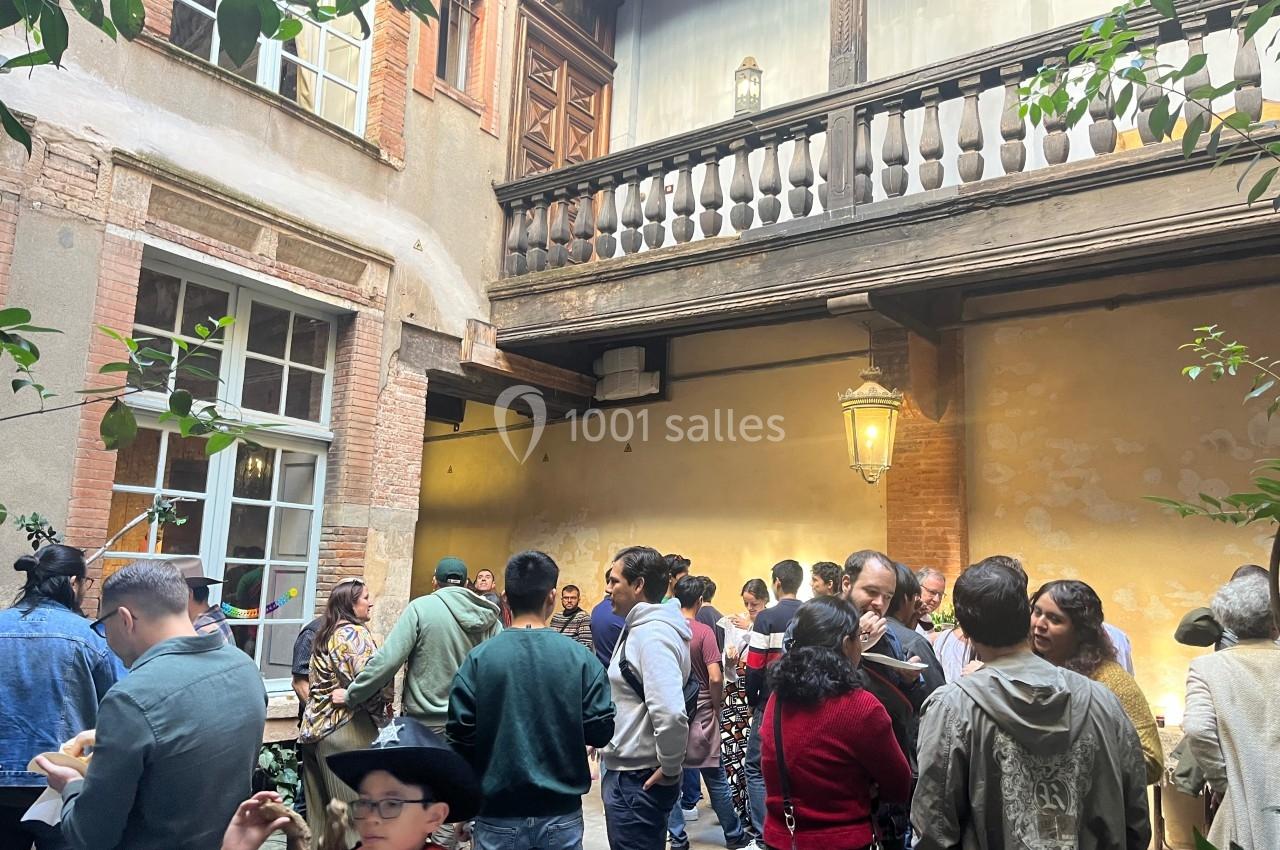 Groupe de personnes discutant dans une cour intérieure avec des murs en briques et un balcon en bois.