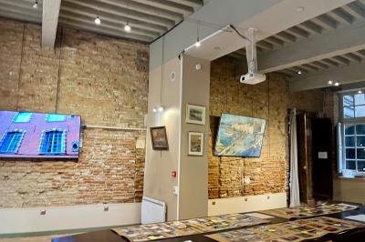 Grande table en bois dressée avec vaisselle, bougies et décorations, dans une salle au mur de briques et sol en terre cuite.