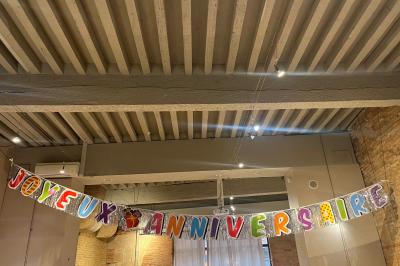 Grande table en bois dressée avec vaisselle, bougies et décorations, dans une salle au mur de briques et sol en terre cuite.