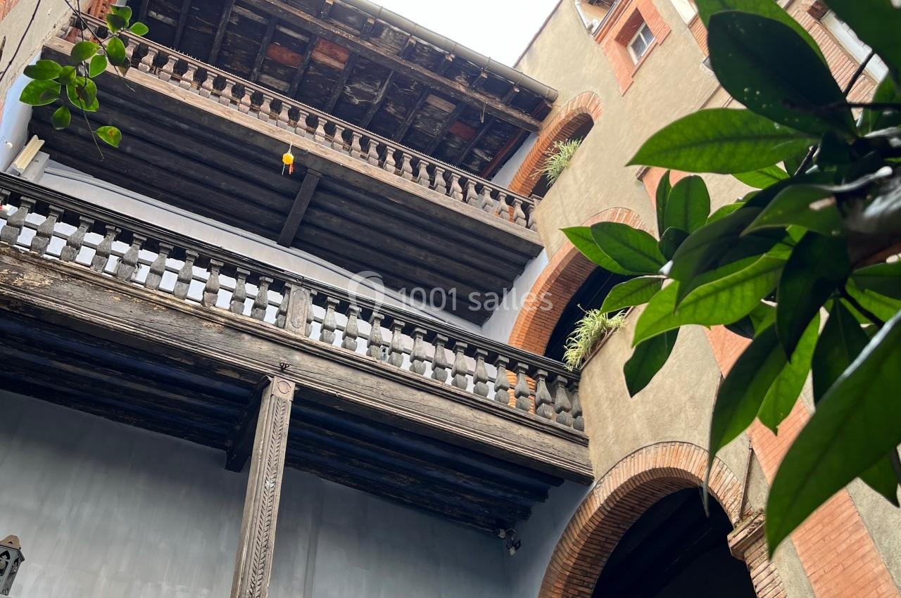 Façade d'un bâtiment ancien avec balcons en bois sculpté, vue en contre-plongée à travers des feuillages.