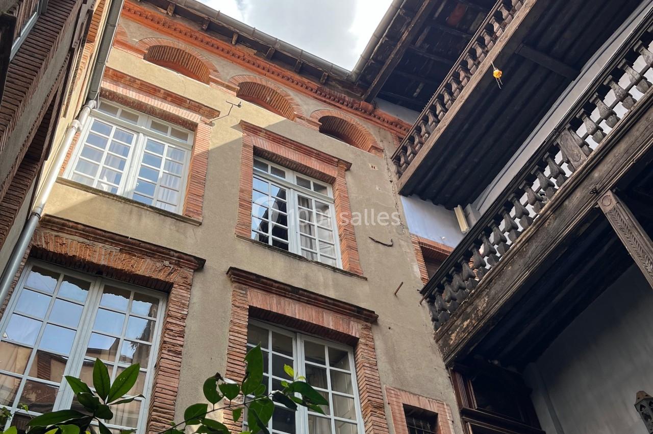 Cour intérieure avec façades en briques, grandes fenêtres et balcons en bois sous un ciel partiellement nuageux.