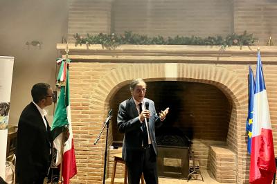 Grande table en bois dressée avec vaisselle, bougies et décorations, dans une salle au mur de briques et sol en terre cuite.