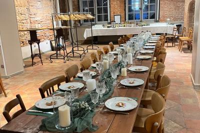 Grande table en bois dressée avec vaisselle, bougies et décorations, dans une salle au mur de briques et sol en terre cuite.
