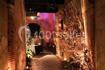 Grande table en bois dressée avec vaisselle, bougies et décorations, dans une salle au mur de briques et sol en terre cuite.