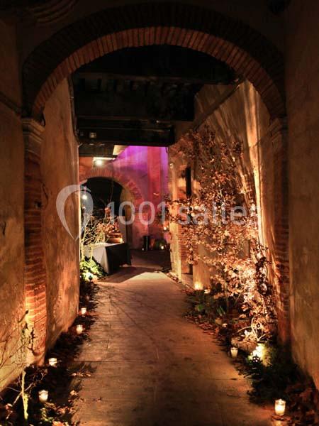 Passage étroit en pierre éclairé par des lumières tamisées, décoré de plantes et de bougies au sol.