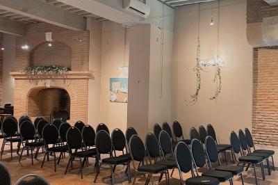 Cour intérieure pavée avec des plantes en pots, entourée de murs en briques et fenêtres à carreaux.