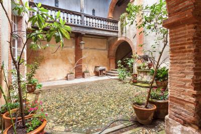 Cour intérieure pavée avec des plantes en pots, entourée de murs en briques et fenêtres à carreaux.