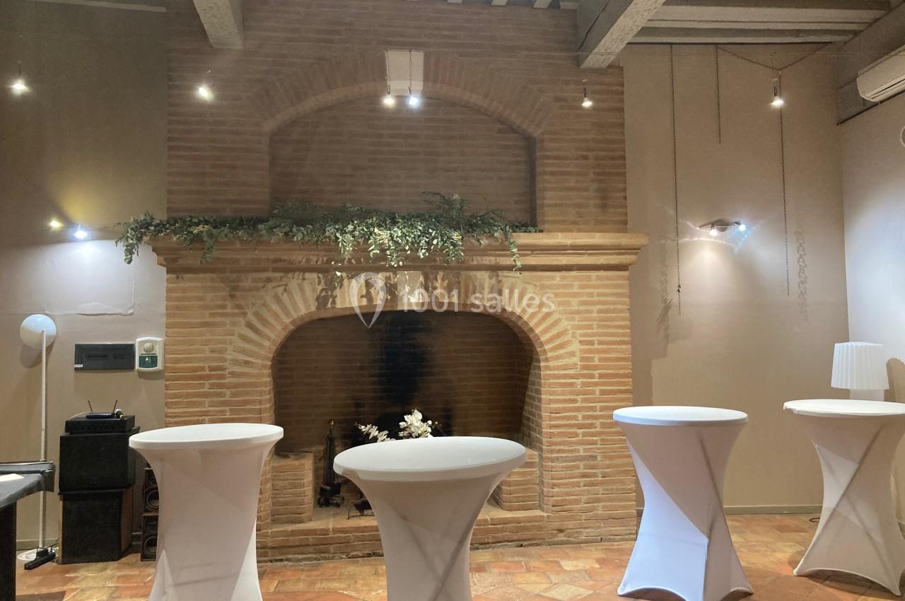 Cheminée en briques dans une salle avec tables hautes drapées de blanc et éclairage tamisé.