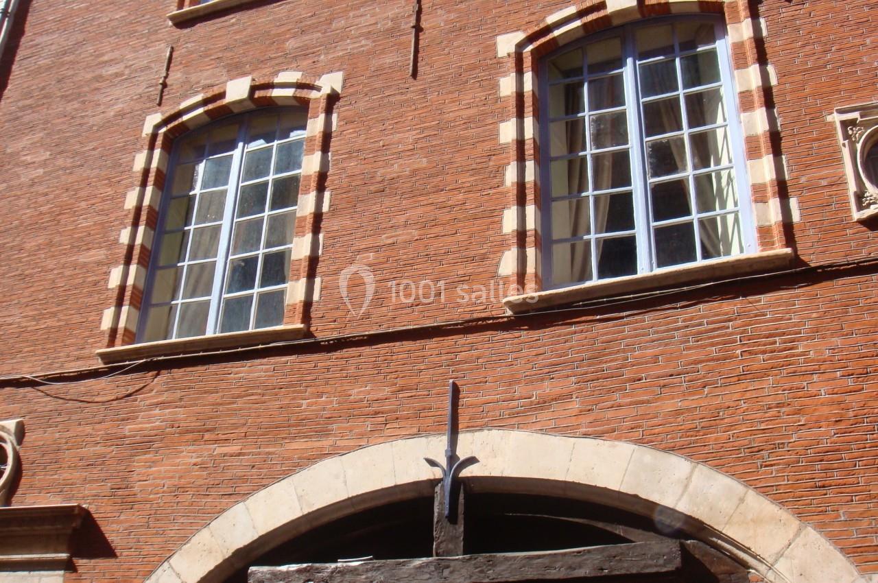 Façade en briques rouges avec fenêtres à encadrement clair et arche en pierre au rez-de-chaussée.