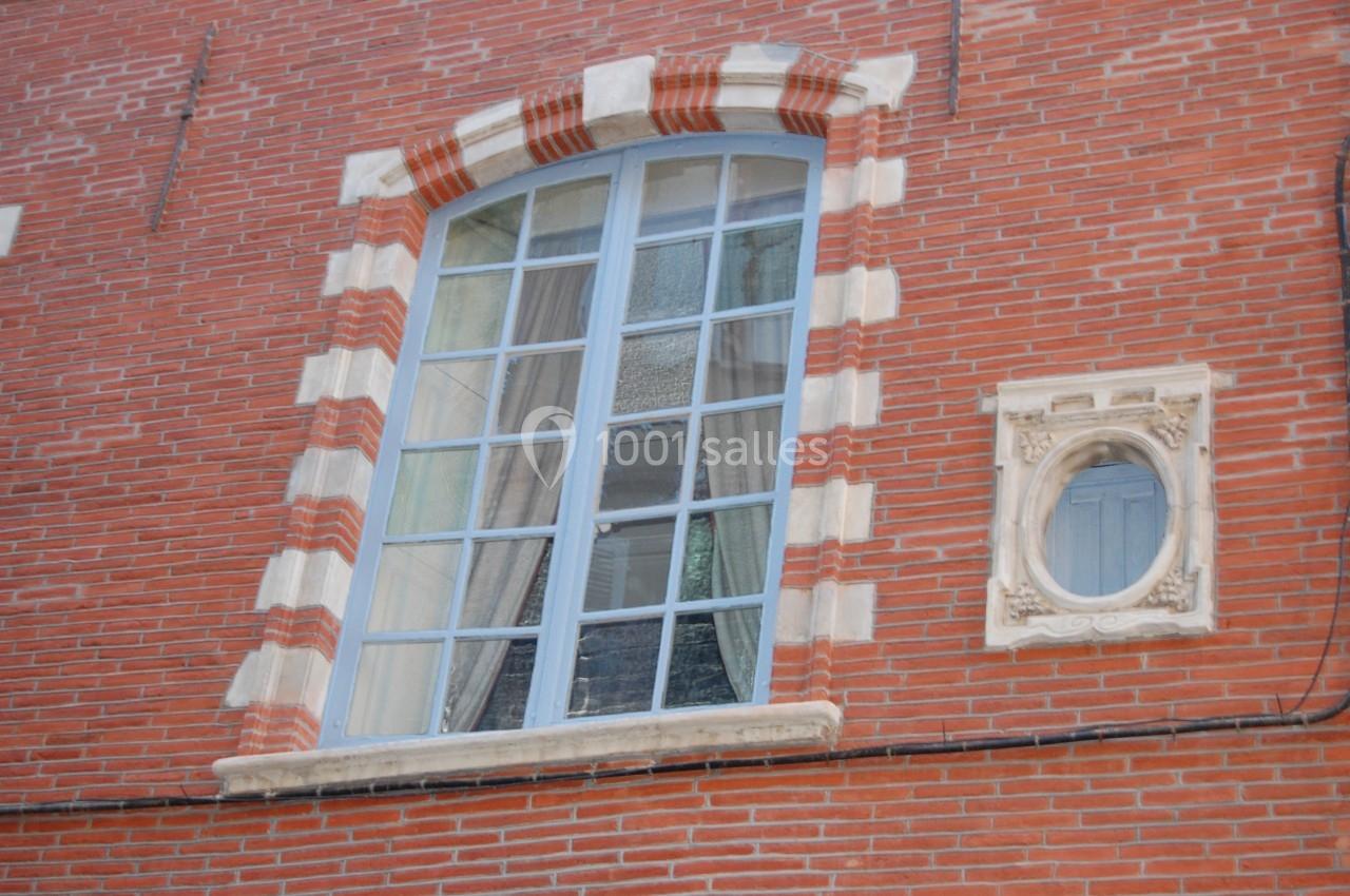 Fenêtre à croisillons avec encadrement en briques et pierre blanche, située sur une façade en briques rouges.