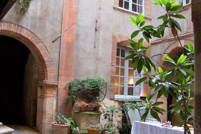 Cour intérieure pavée avec des plantes en pots, entourée de murs en briques et fenêtres à carreaux.