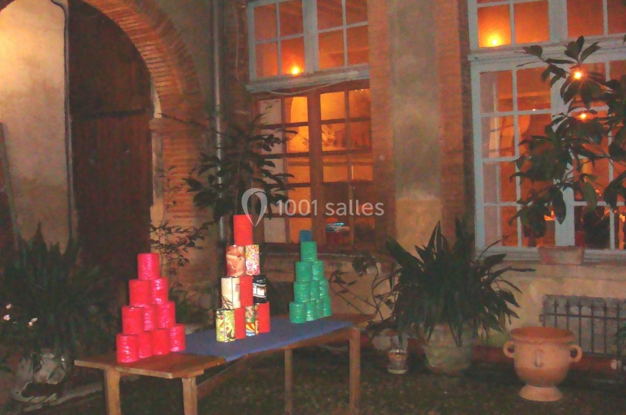 Table avec des boîtes colorées empilées dans une cour intérieure éclairée, entourée de plantes et de fenêtres.