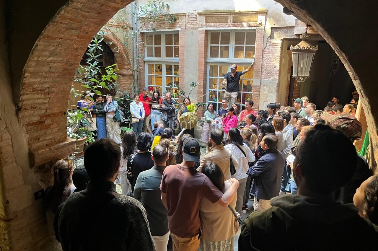 Un groupe de personnes rassemblées dans une cour intérieure, observant une scène sous une arche en briques.