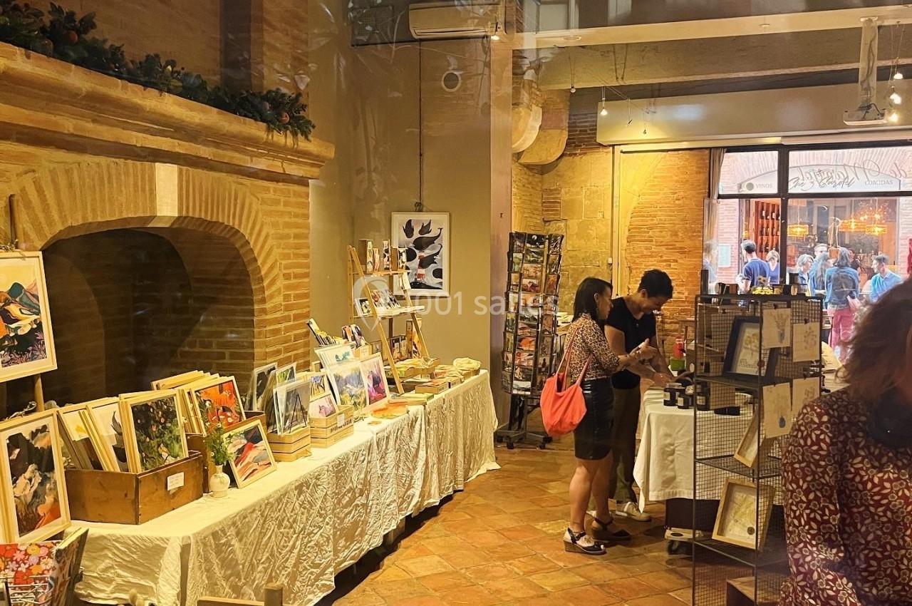 Vue intérieure d'une boutique artisanale avec des tables exposant des œuvres d'art et des clients discutant.