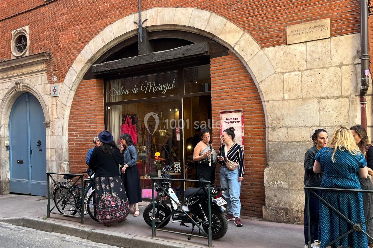 Devanture d'un salon avec des personnes discutant sur le trottoir, vélos et scooters stationnés devant.