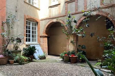 Cour intérieure pavée avec des plantes en pots, entourée de murs en briques et fenêtres à carreaux.