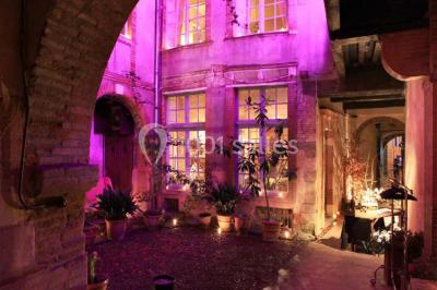Cour intérieure pavée avec des plantes en pots, entourée de murs en briques et fenêtres à carreaux.