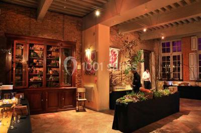 Cour intérieure pavée avec des plantes en pots, entourée de murs en briques et fenêtres à carreaux.