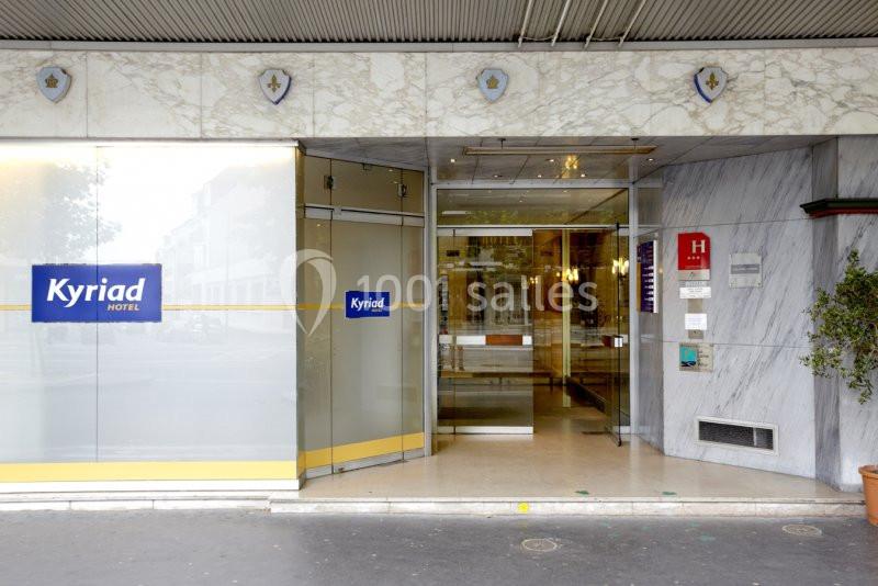 Entrée d'un hôtel avec portes vitrées coulissantes, enseigne visible et décoration en marbre.