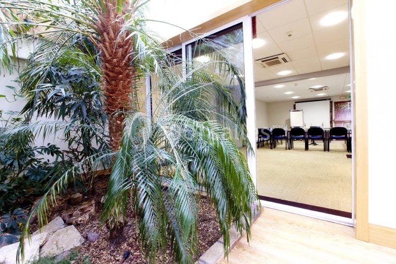 Vue d'une salle de réunion lumineuse avec des chaises alignées, accessible depuis un espace végétalisé intérieur.