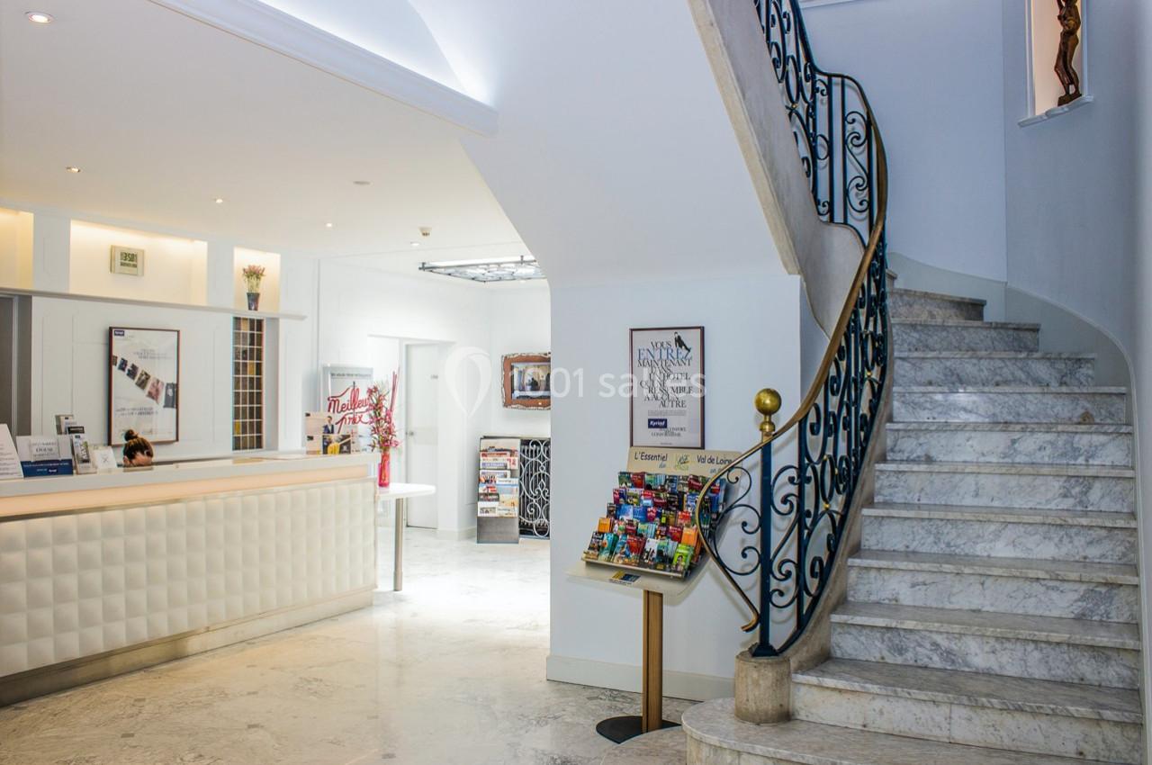 Hall d'entrée lumineux avec comptoir d'accueil, escalier en marbre et présentoir de brochures colorées.