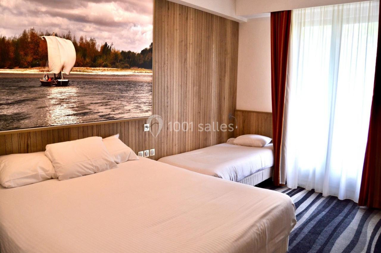 Chambre d'hôtel avec deux lits, un tableau représentant un voilier, et une grande fenêtre avec rideaux.